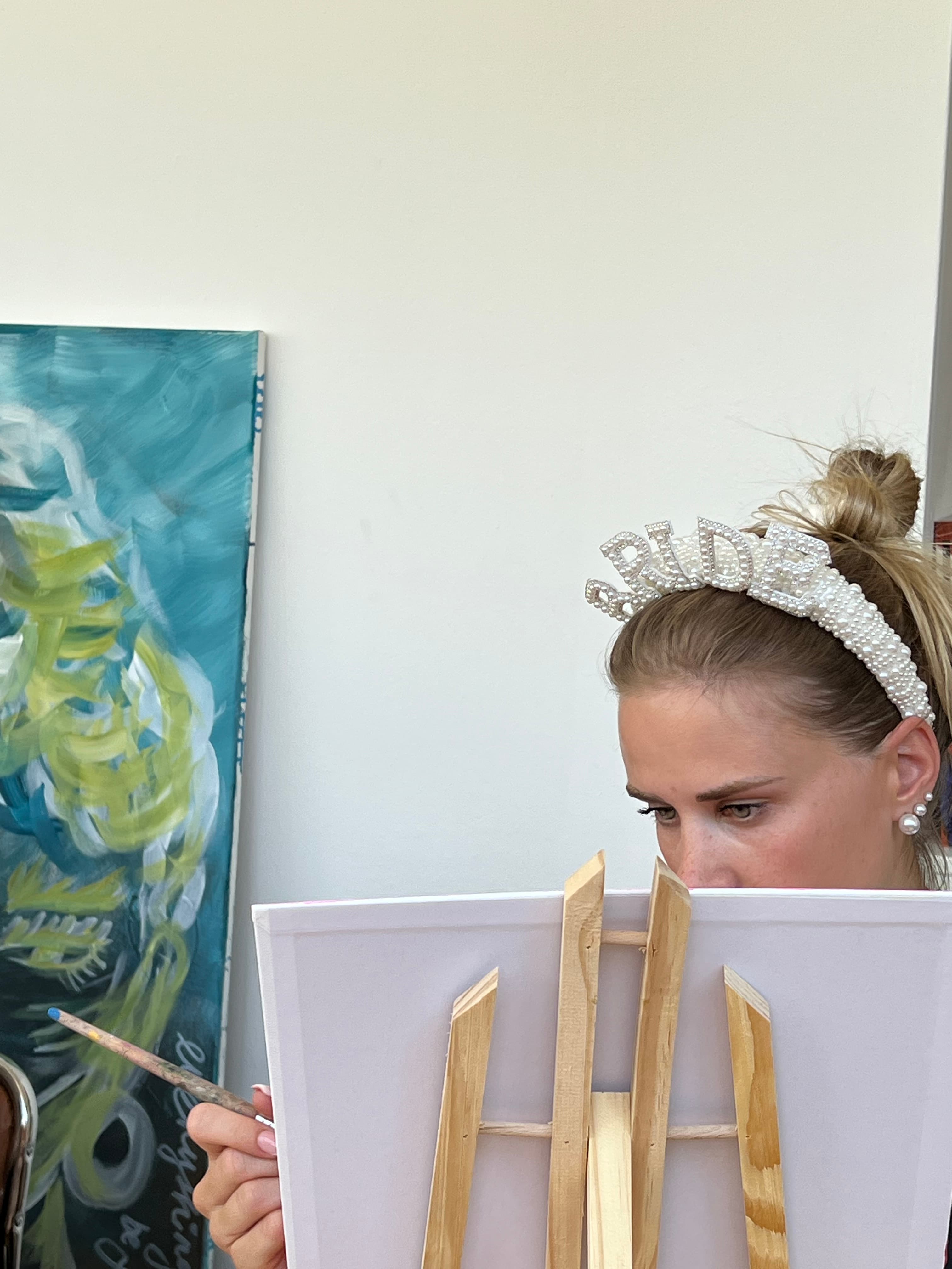 Bride-to-be mit Perlen-Stirnband malt an einer Staffelei — JGA-Stimmung im HeimART Studio