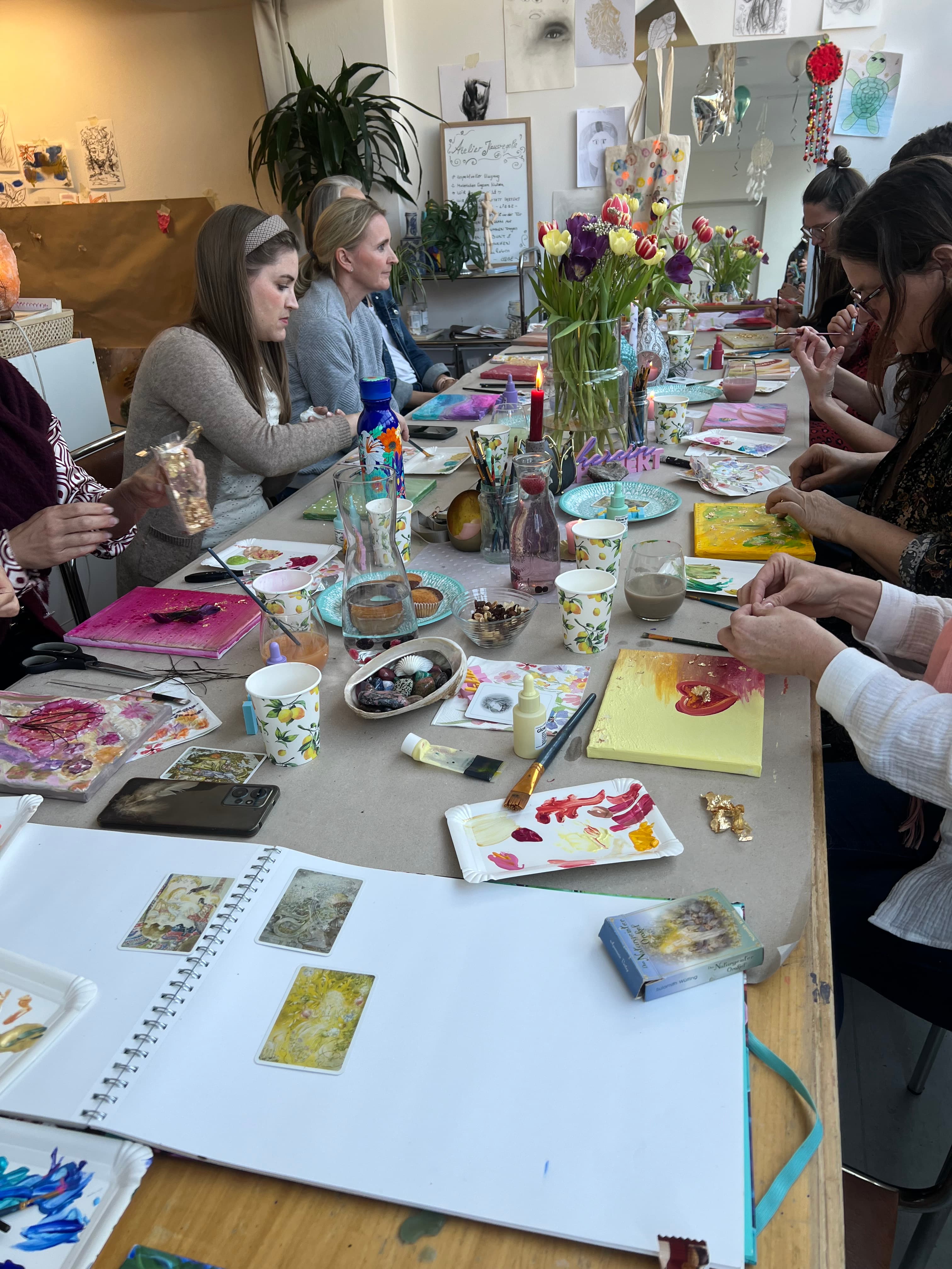 Gruppe Frauen am langen Tisch im HeimART Studio beim gemeinsamen Malen mit Tulpen und vielen fertigen Leinwänden