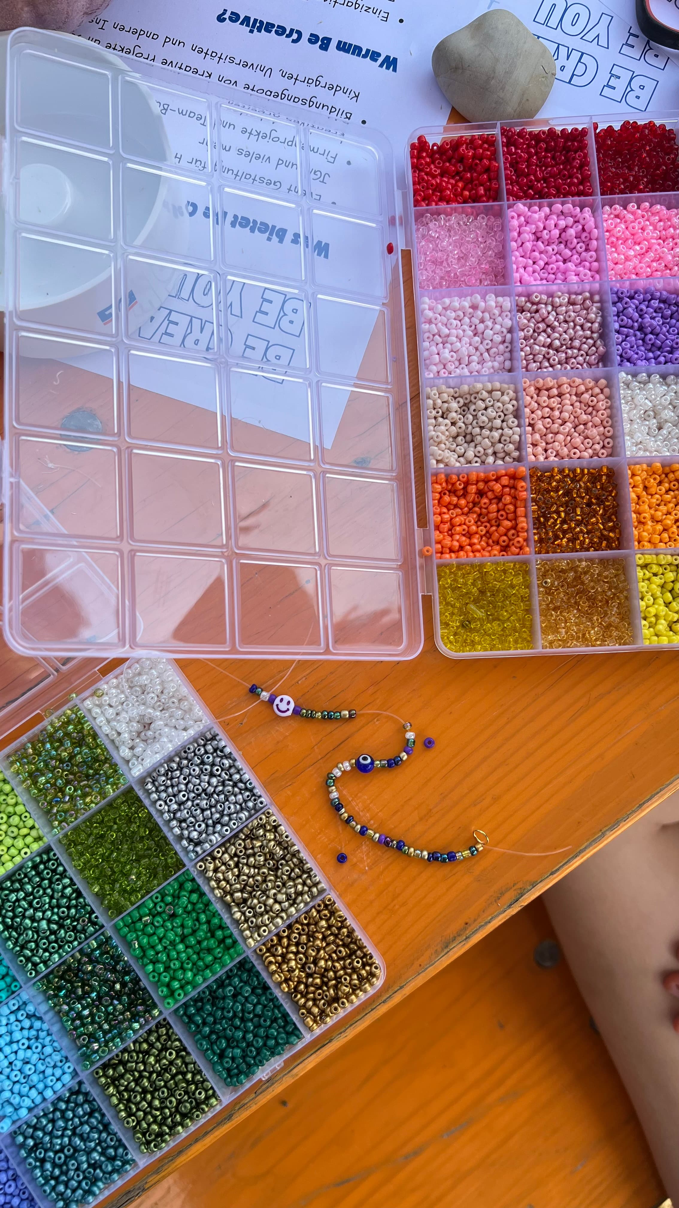 Perlentabletts in Regenbogenfarben für Schmuck, daneben Karten mit Affirmationen und ein angefangenes Armband